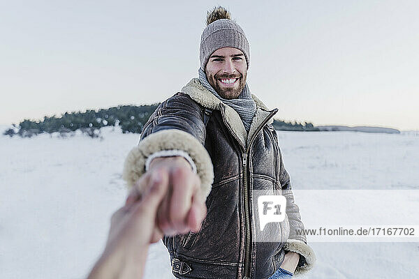 Lächelnder Mann  der die Hand einer Frau hält  während er im Schnee vor einem klaren Himmel steht