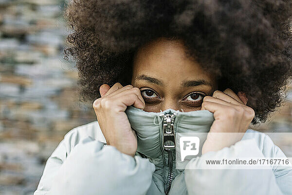 Afro young woman holding winter coat on face outdoors