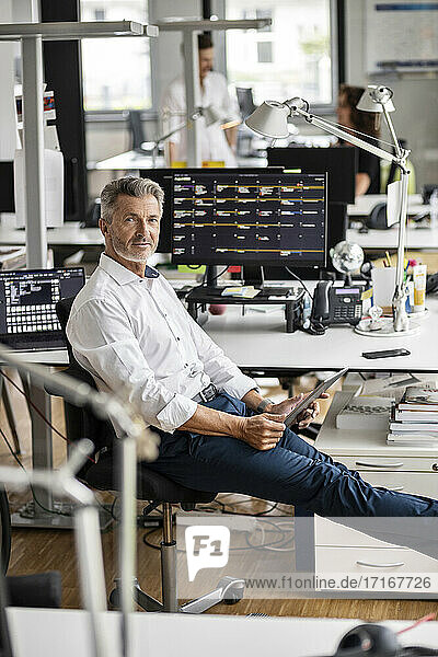Selbstbewusster reifer Geschäftsmann  der ein digitales Tablet hält  während er im Büro sitzt