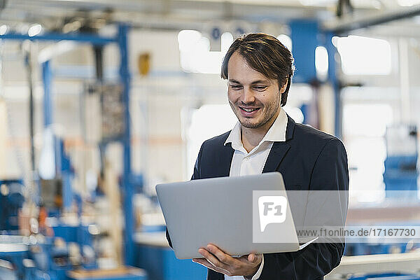 Smiling businessman using laptop while standing at industry