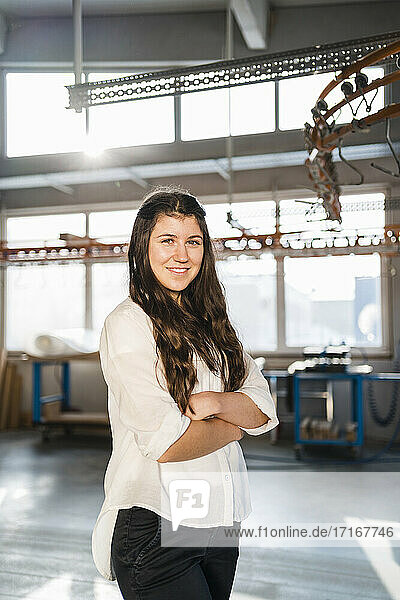 Confident businesswoman smiling while standing with arms crossed at industry