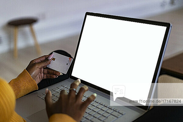 Young woman holding credit card while using laptop doing online shopping at home