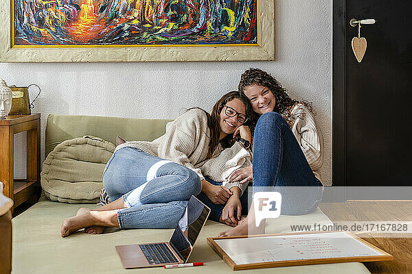 Lächelnde Freundinnen  die mit Laptop und Schiefertafel zu Hause auf einer Matratze sitzen