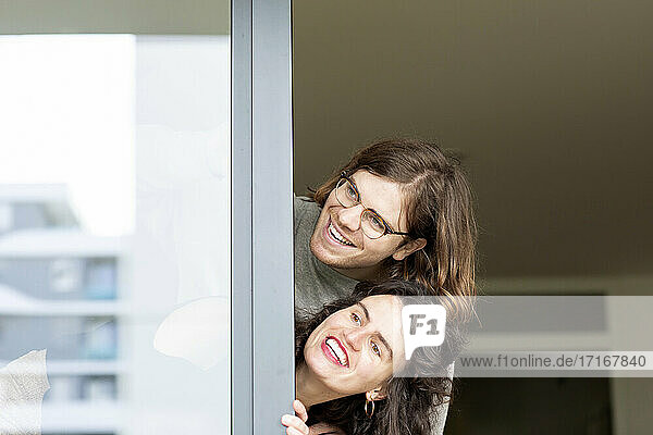 Cheerful couple peeking through glass window