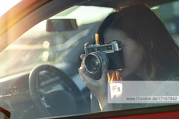 Young woman photographing through old-fashioned camera from car while travelling