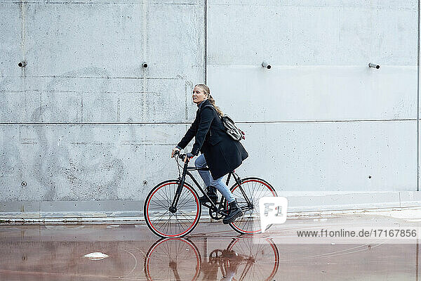 Woman doing cycling on wet road by wall