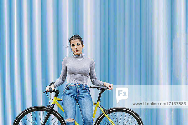 Selbstbewusste Frau im mittleren Erwachsenenalter sitzt auf einem Fixie-Fahrrad vor einer blauen Wand