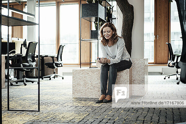 Unternehmerin  die ihr Smartphone benutzt  während sie auf einer Stützmauer im Büro sitzt