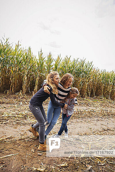 Friends playing together while standing against corn field