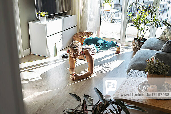 Frau übt die Plank-Position  während sie zu Hause auf dem Boden trainiert