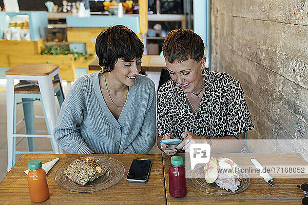 Frau  die ein Mobiltelefon benutzt  während sie im Restaurant neben einem Freund sitzt