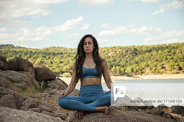 Junge Frau meditiert im Schneidersitz auf einem Felsen sitzend