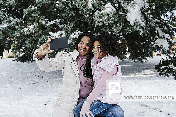 Happy mother and daughter taking selfie on smart phone in park