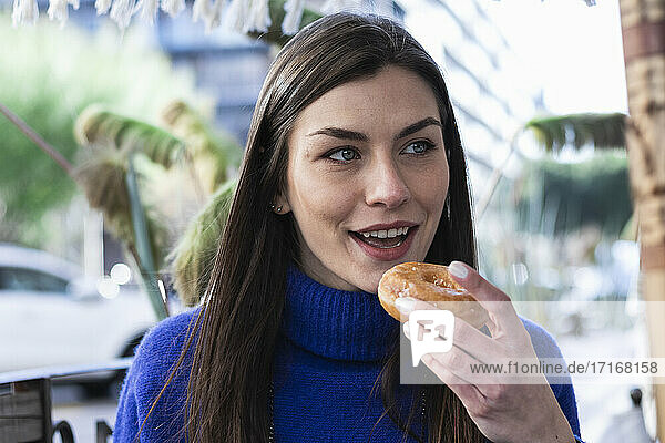 Beautiful woman looking away while eating donut in sidewalk cafe