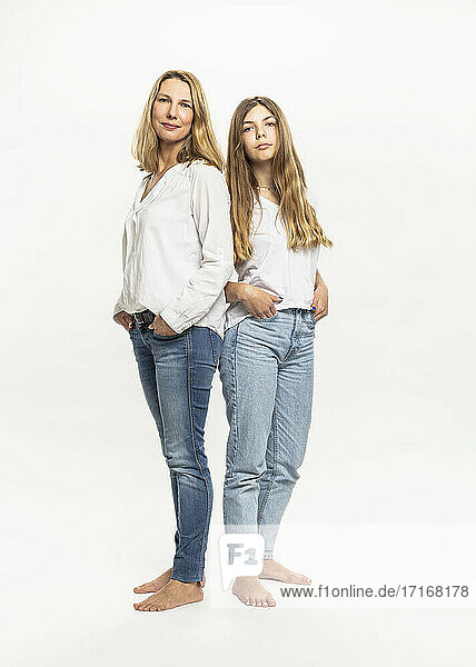 Mother and daughter with hands in pockets standing against white background