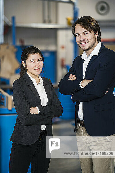 Young confident business people smiling while standing with arms crossed at industry
