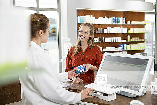 Female pharmacist giving medicine to woman at checkout in store