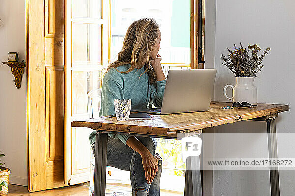 Thoughtful female freelancer looking away while sitting at home office