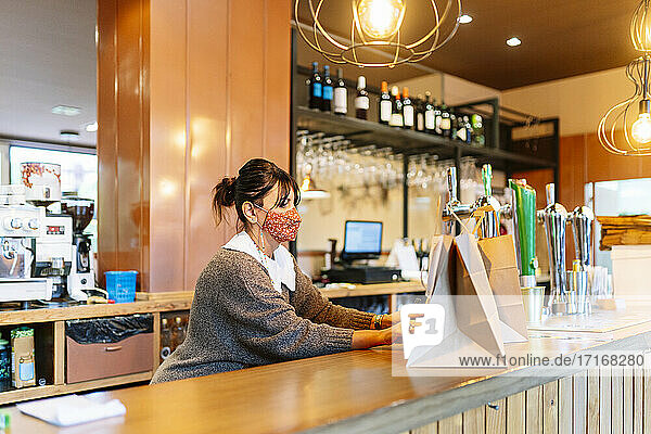Weiblicher Besitzer hält Essen zum Mitnehmen in einer braunen Tüte auf dem Restauranttisch bereit