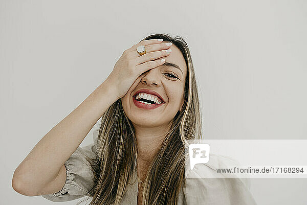 Smiling woman with hand covering eye against white background