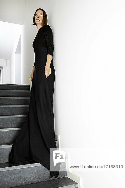 Woman in black dress leaning on wall while standing on staircase