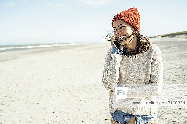 Portrait of woman wearing knit hat talking on smart phone at beach