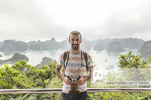 Smiling man with vintage camera standing on observation point against Halong bay  Vietnam