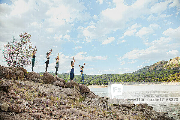 Junge Frauen üben Yoga mit Lehrer auf einem Felsen gegen den Himmel