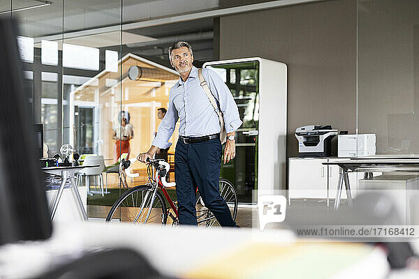 Mature businessman with bag and bicycle leaving after work from office