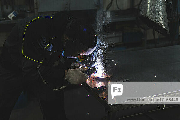 Young welder working with welding torch at workshop