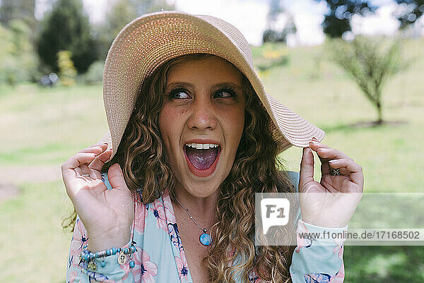 Excited young woman looking sideways while wearing sun hat at park during sunny day