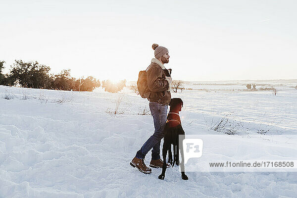 Male backpacker standing with Great Dane dog while looking away in snow
