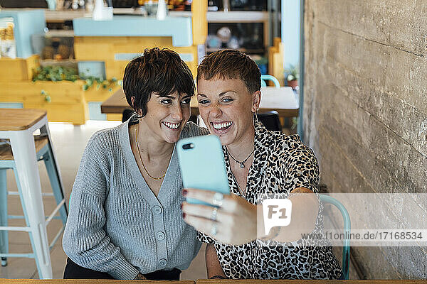 Junge Freunde lächelnd während der Aufnahme von Selfie durch Handy sitzen im Restaurant