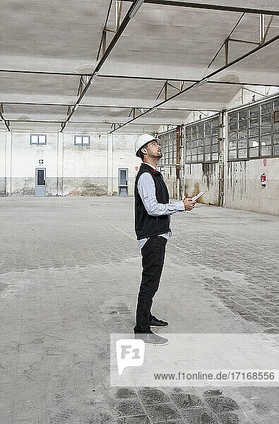 Männlicher Architekt mit Karte  der beim Bau eines Gebäudes nachdenklich nach oben schaut
