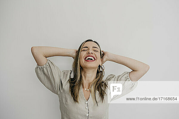 Laughing woman with hands behind head against white background