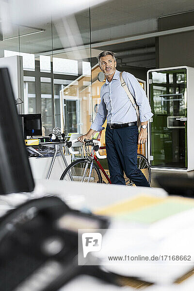Geschäftsmann mit Fahrrad und Tasche schaut beim Gehen im Büro weg