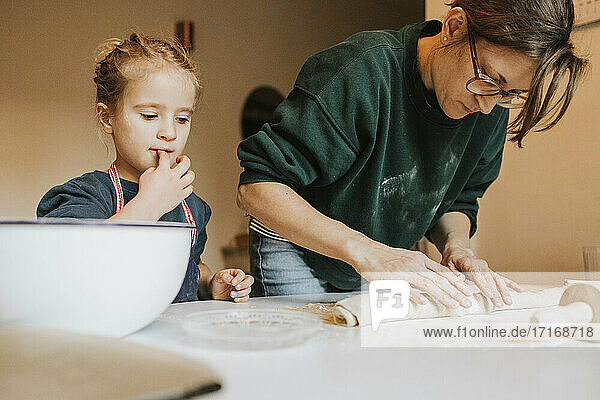 Mother rolling cinnamon roll dough with daughter at home