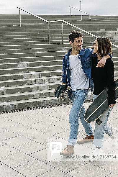 Young couple with skateboards walking near steps