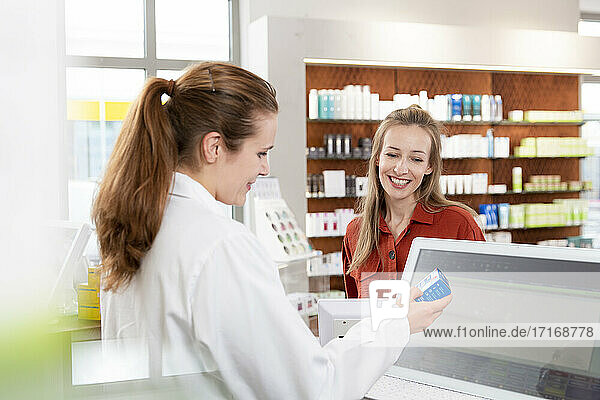 Female pharmacist reading instructions on medicine while woman standing at checkout