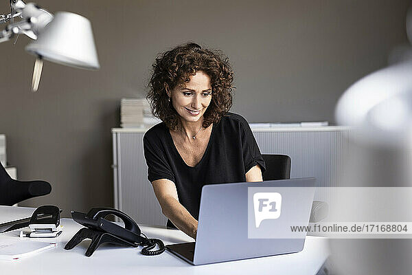 Lächelnde Geschäftsfrau  die an einem Laptop arbeitet  während sie am Schreibtisch im Büro sitzt