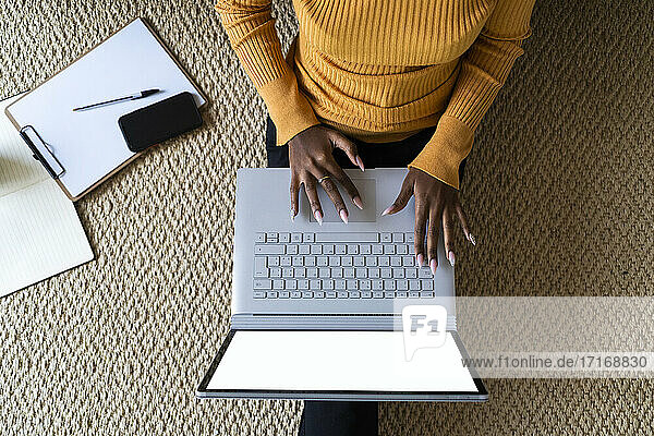 Young woman using laptop while sitting on carpet at at home