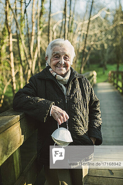 Lächelnde ältere Frau auf einer Fußgängerbrücke mit Gesichtsschutzmaske während COVID-19