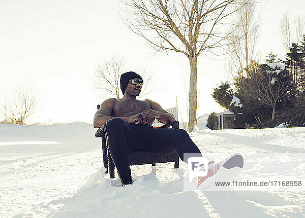 Shirtless sportsman relaxing while sitting on chair during winter