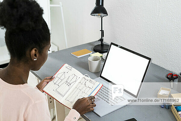 Modestylistin mit Laptop  die zu Hause sitzend ein Diagramm in einem Buch analysiert