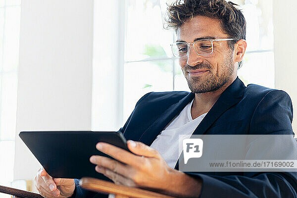 Lächelnder Geschäftsmann  der ein digitales Tablet benutzt  während er zu Hause sitzt
