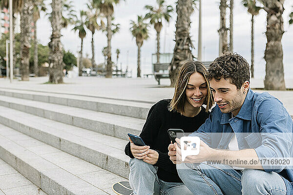 Smiling couple looking at smart phones outdoors