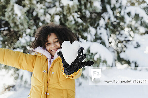 Nettes Mädchen zeigt herzförmigen Schnee  während sie im Park steht