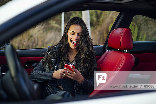 Aufgeregte Frau  die im Auto sitzend ein Mobiltelefon benutzt