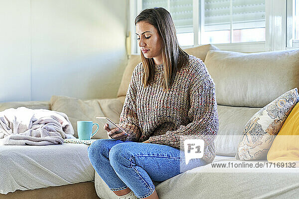 Female in warm clothing using smart phone on sofa at home