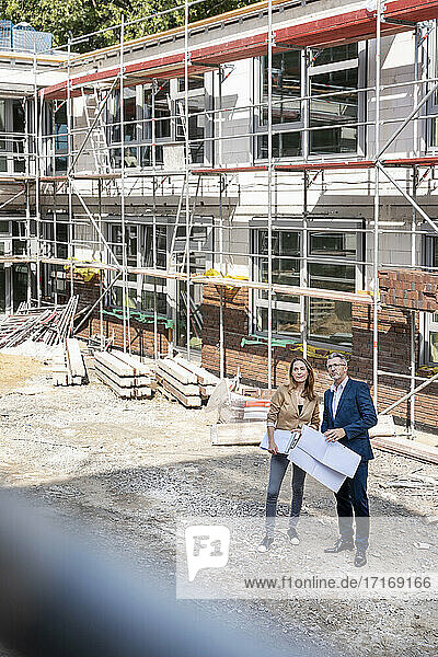 Männlicher Ingenieur hält Papier  während er mit einer Geschäftsfrau auf einer Baustelle arbeitet